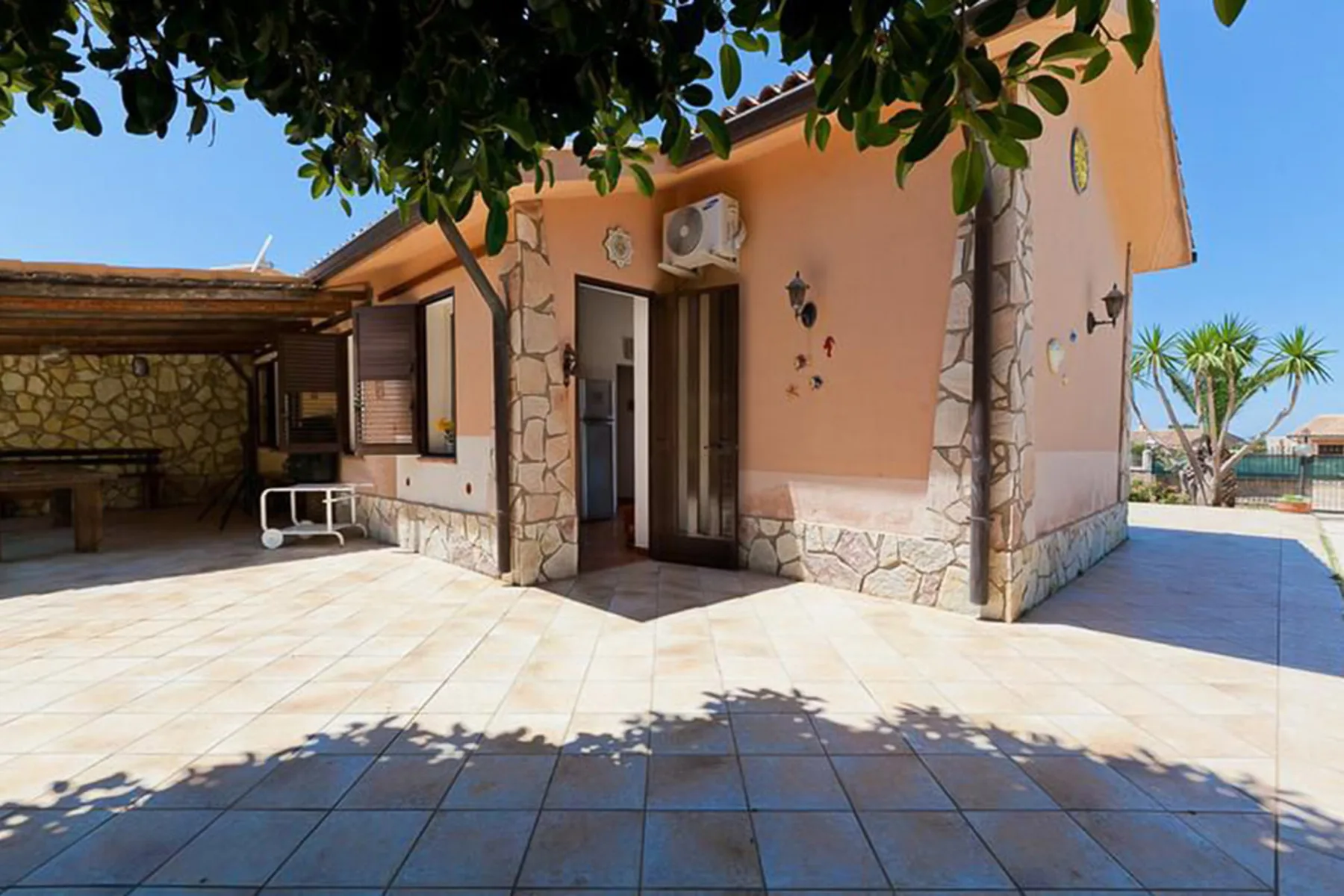 A tiled outdoor patio beside a peach-colored building and shaded seating area.