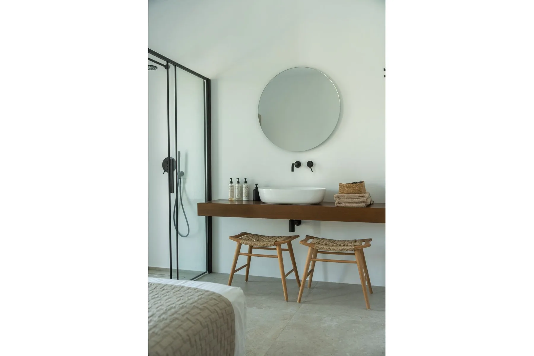 A modern bathroom with a round mirror, wall-mounted sink, and glass shower.