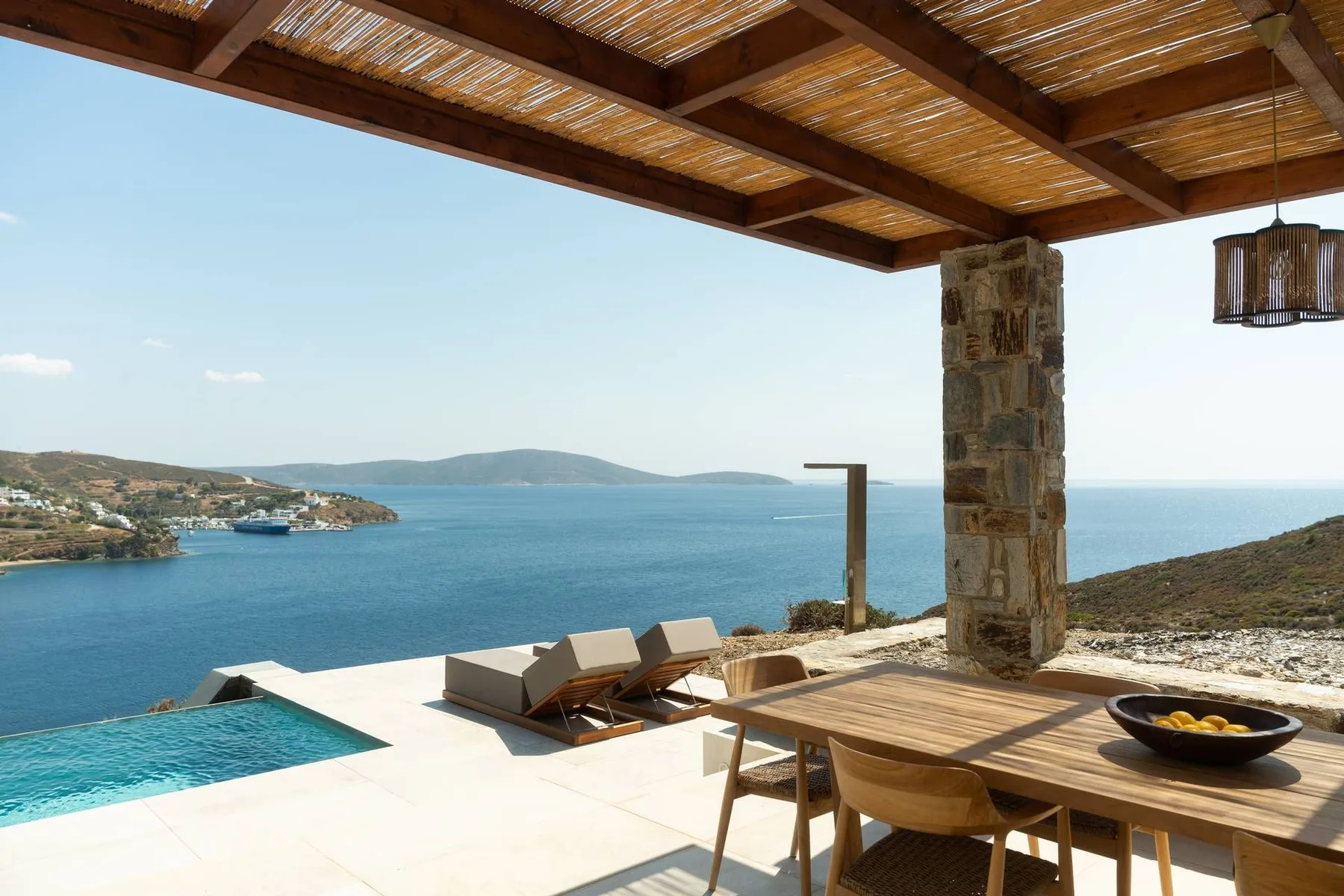 A seaside terrace with a dining table, lounge seating, and a pool overlooking the water.