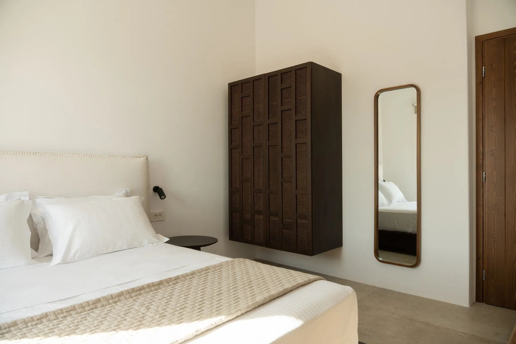 A bedroom with a bed, dark wall cabinet, and full-length mirror.