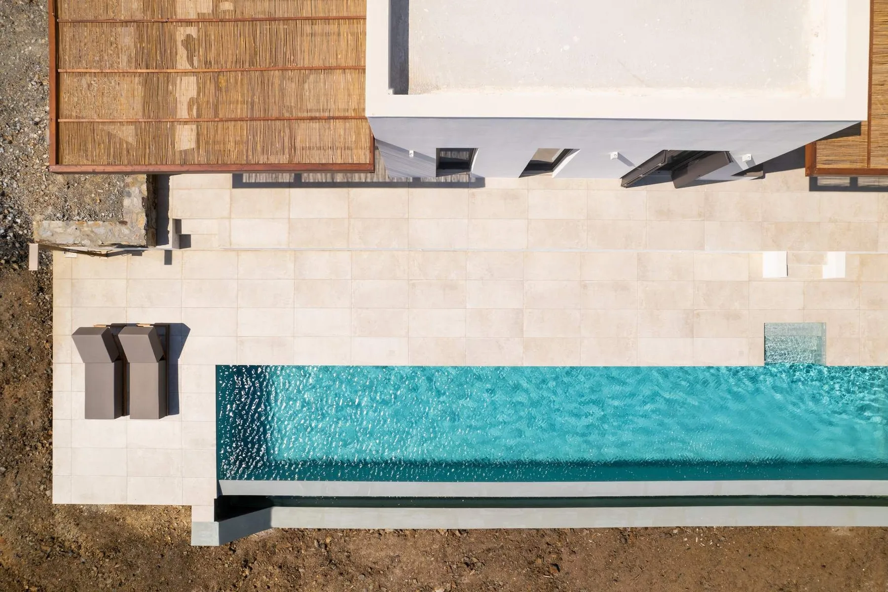 An overhead view of a swimming pool beside a paved patio and building.