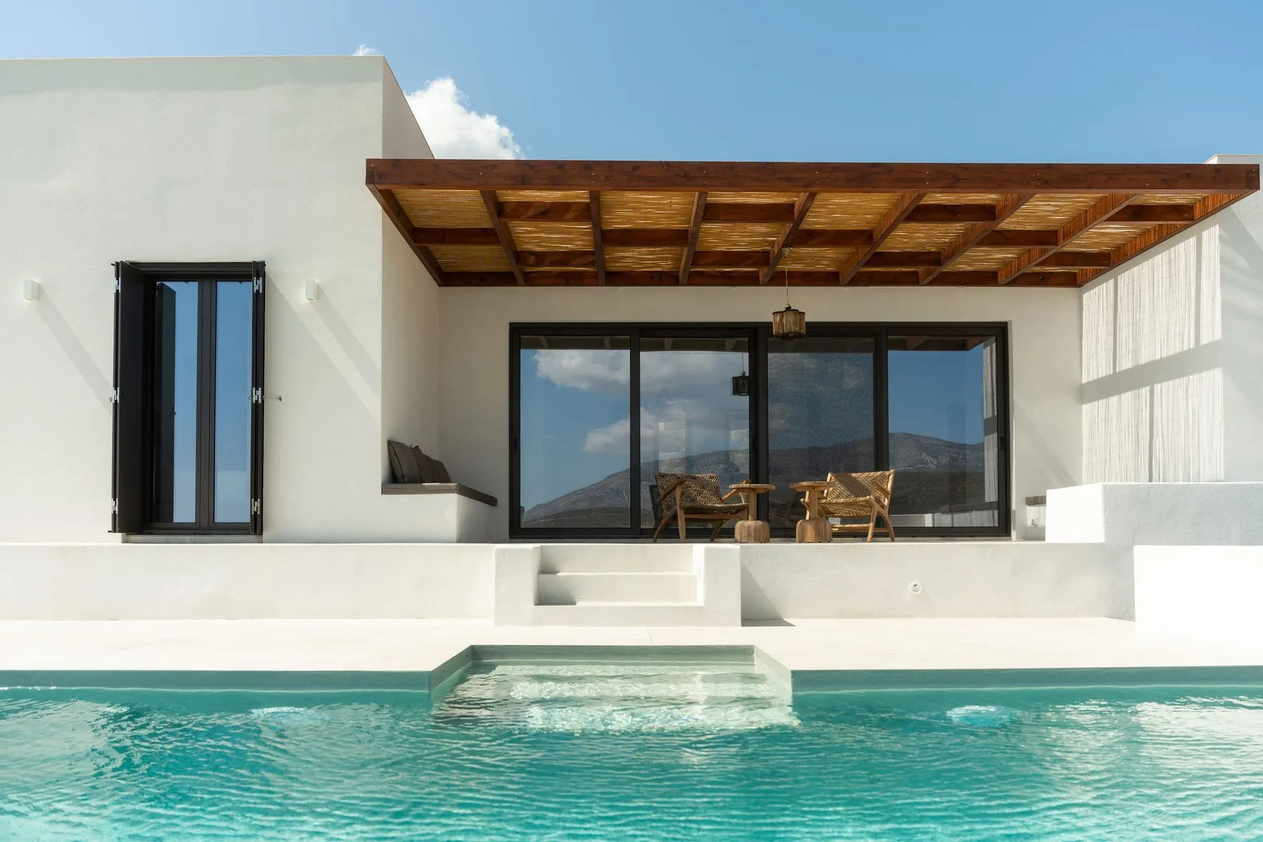 A modern white house opens onto a turquoise swimming pool.