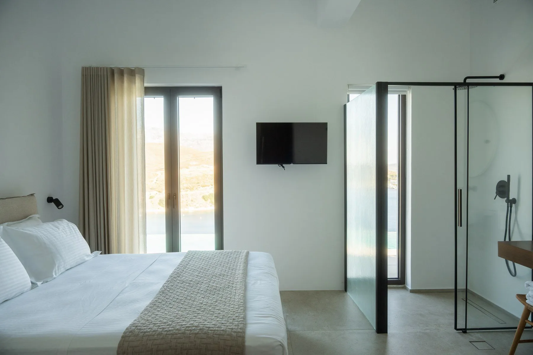A bright bedroom with a bed, wall-mounted television, and glass shower.