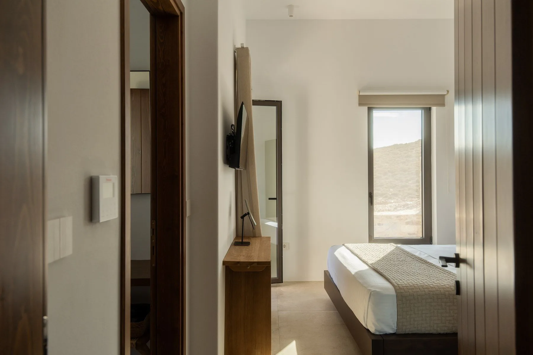A bedroom with a bed and a window overlooking a sunlit hillside.