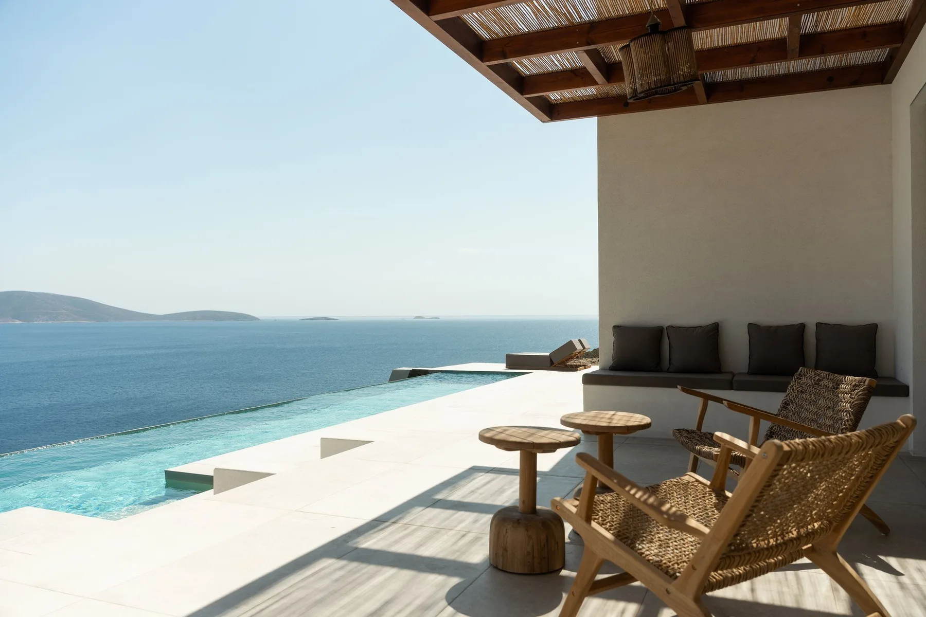 A seaside terrace overlooks the water, with outdoor seating beside a pool.