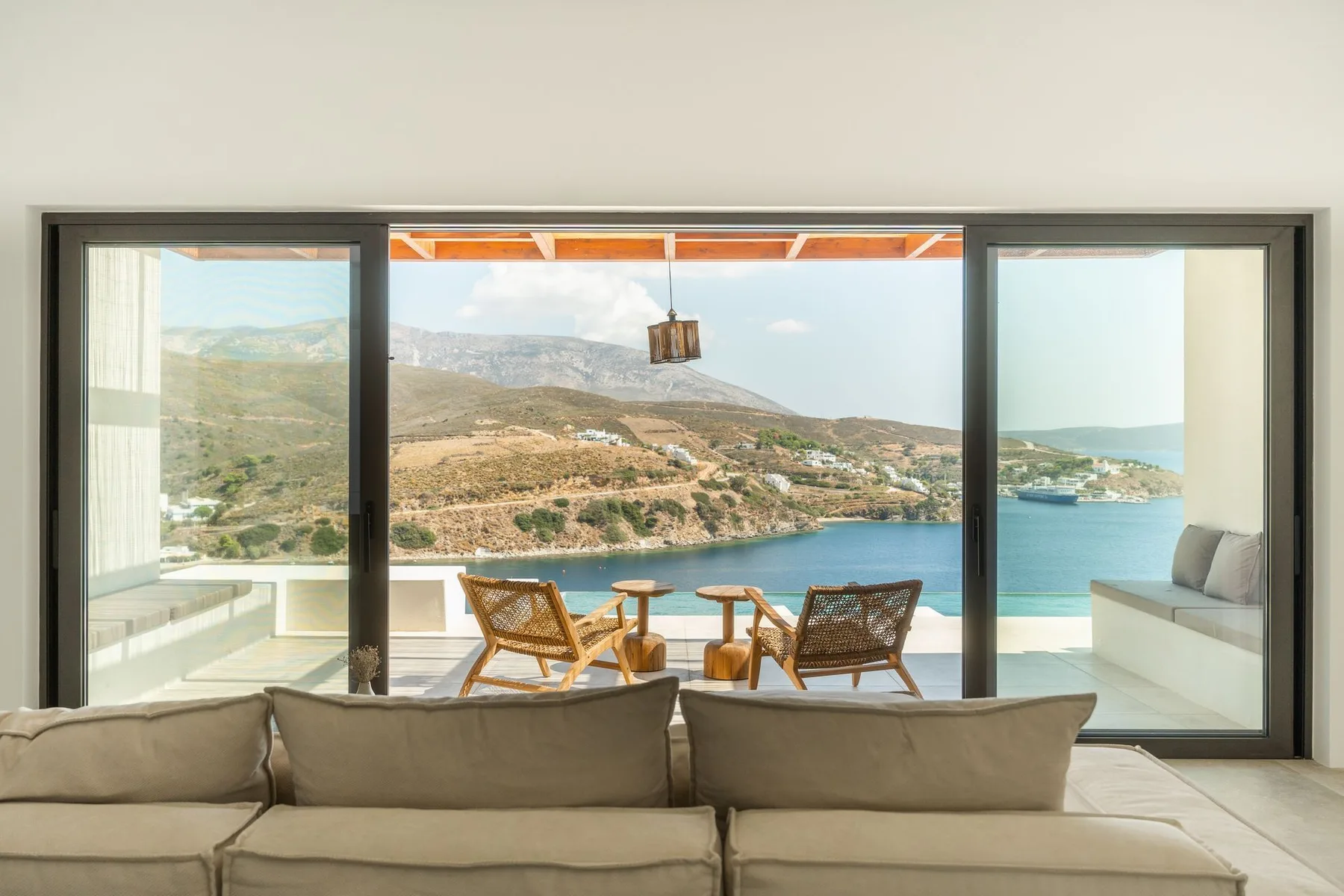 A living room opens onto a terrace with seating and a coastal view.