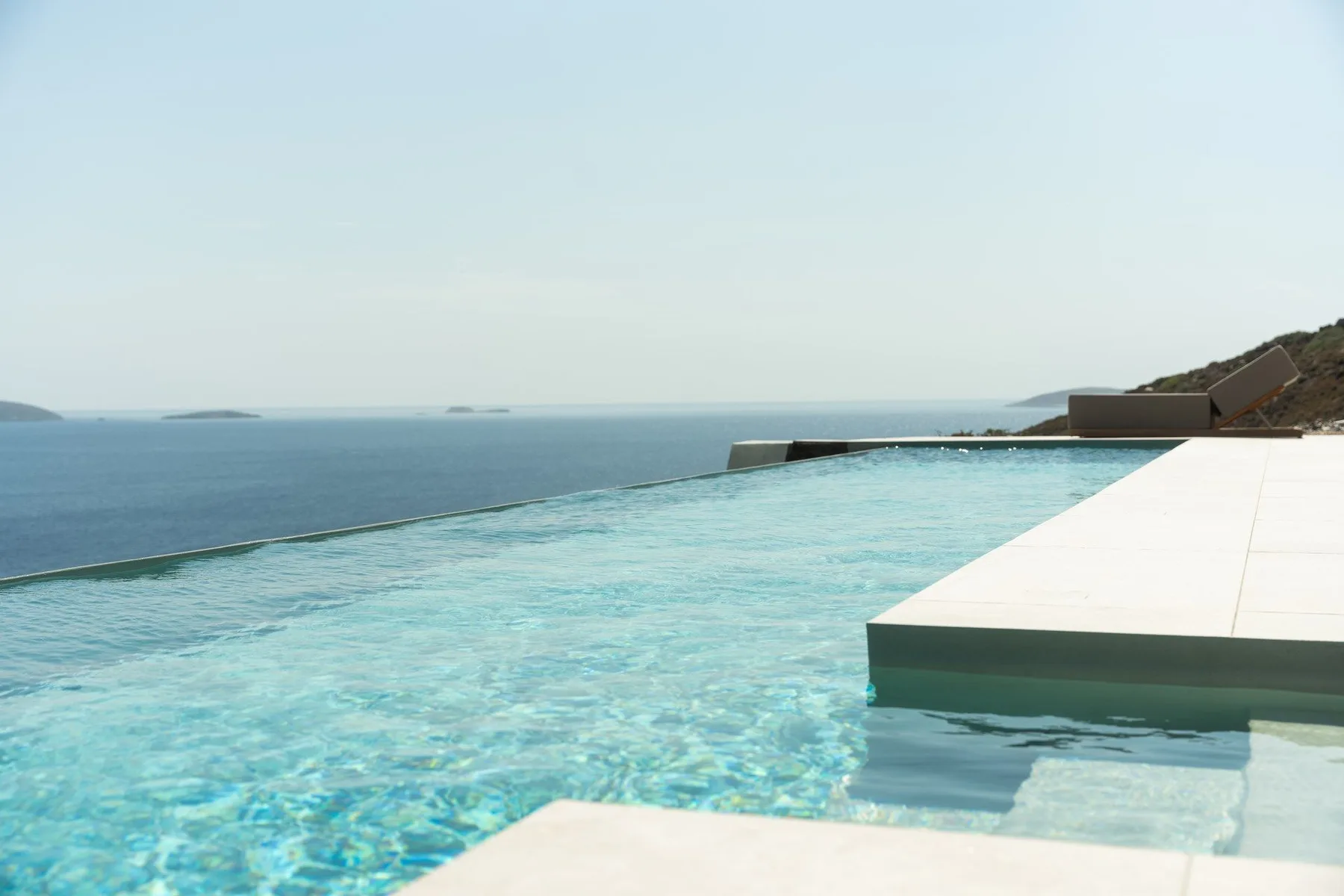 An infinity pool overlooks the sea beneath a clear sky.