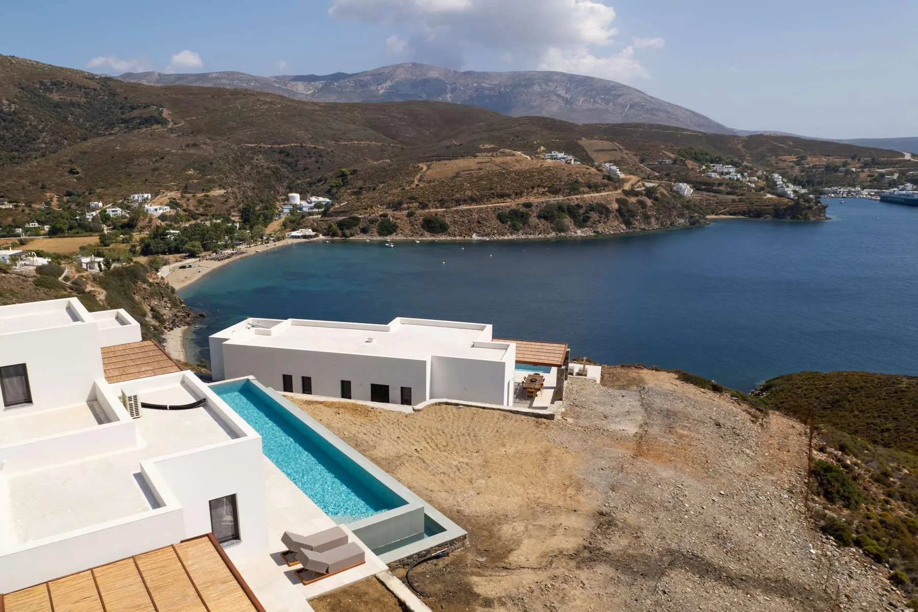 White buildings and a long pool overlook a bay and surrounding hills.
