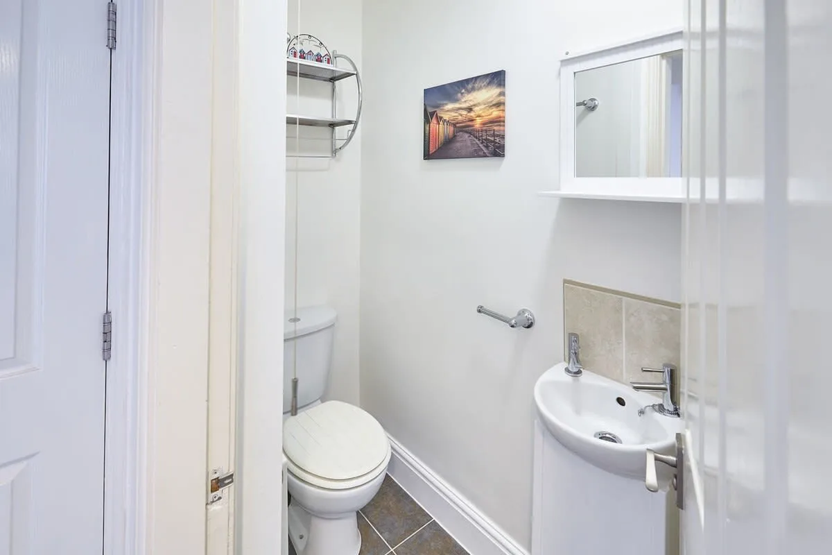 A compact bathroom with a toilet, pedestal sink, and framed wall art.
