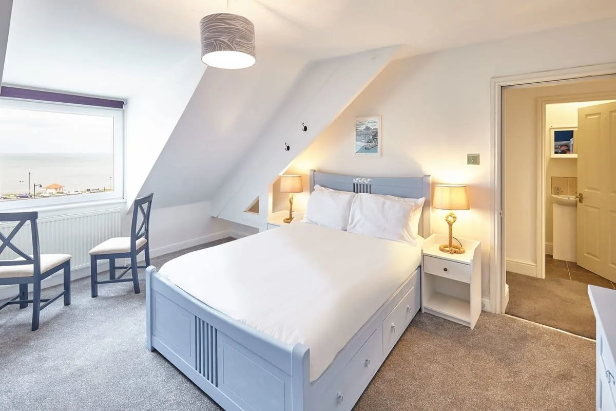 A bright bedroom with a bed beneath a sloped ceiling and a window.