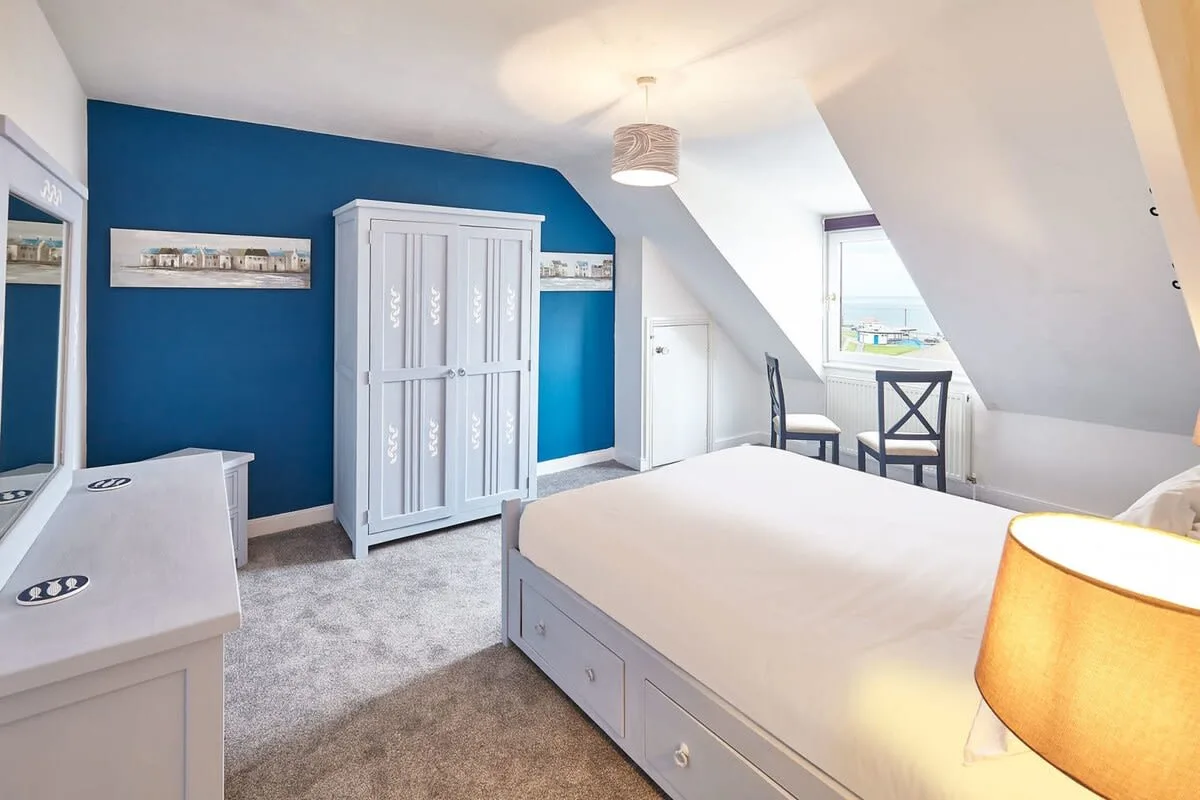 A bright bedroom with a bed, blue accent wall, and sloped ceiling.