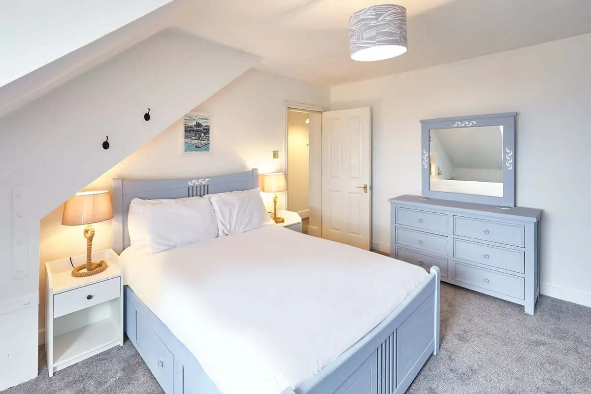 A bright bedroom with a bed, bedside tables, and a dresser with mirror.