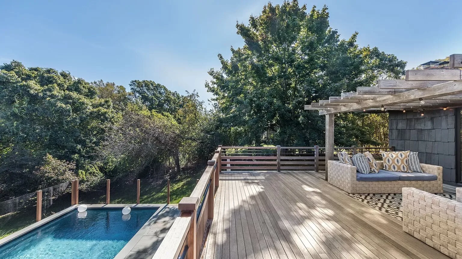 Una terraza exterior con asientos junto a una piscina, rodeada de árboles.