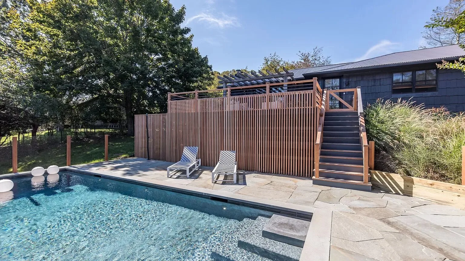 A backyard pool sits beside a raised wooden deck and outdoor seating.
