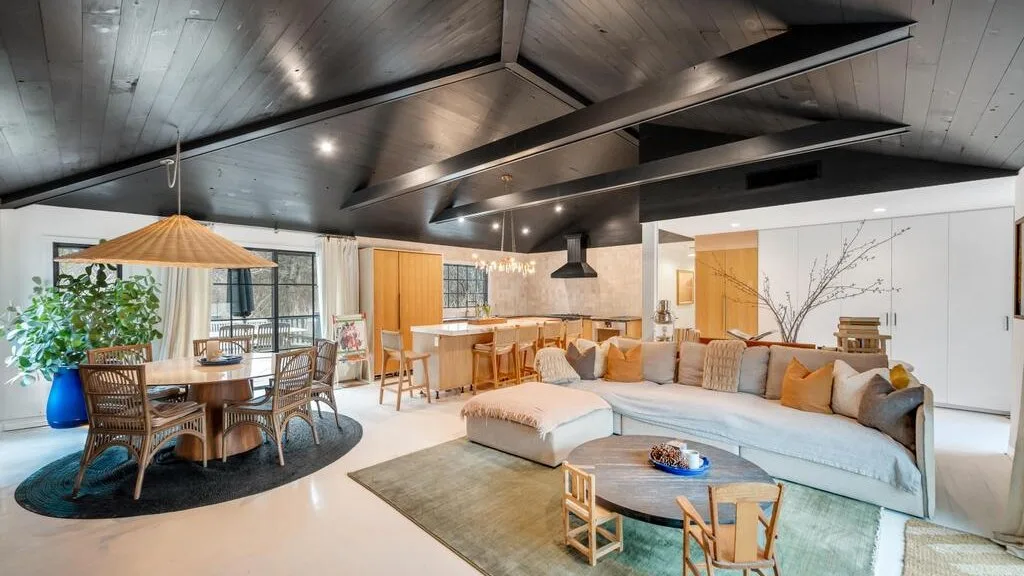 A spacious living and dining area with light seating beneath a dark exposed-beam ceiling.
