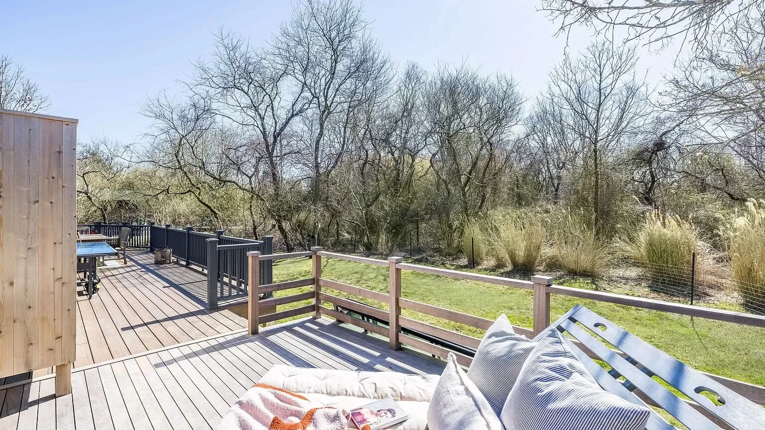 An outdoor wooden deck with seating overlooks trees and tall grasses.