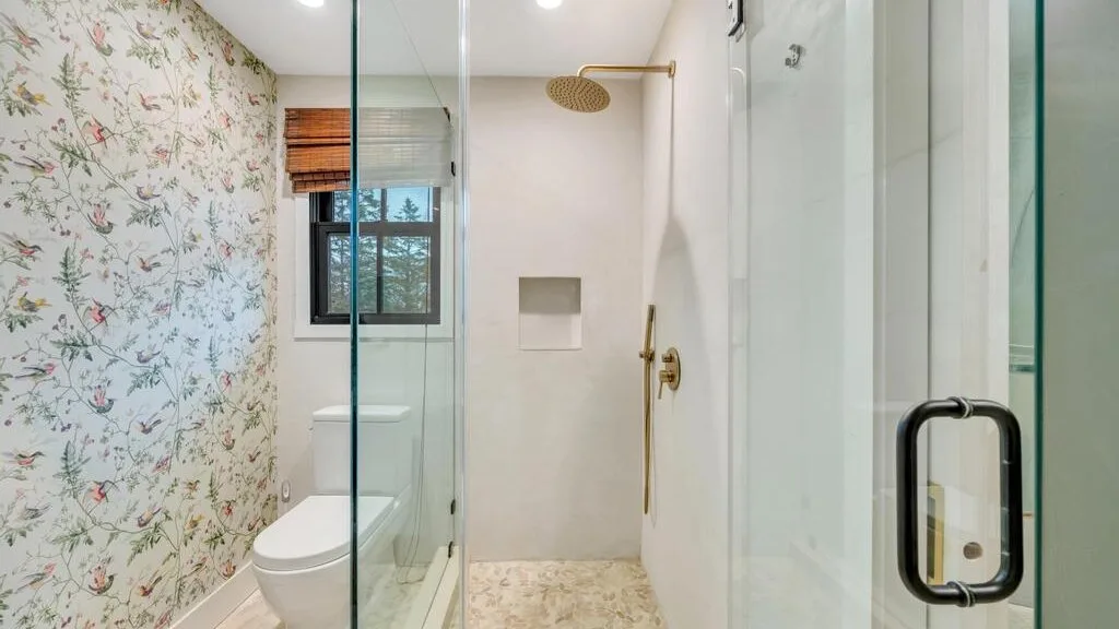 A bathroom with a glass shower and floral-patterned wallpaper.