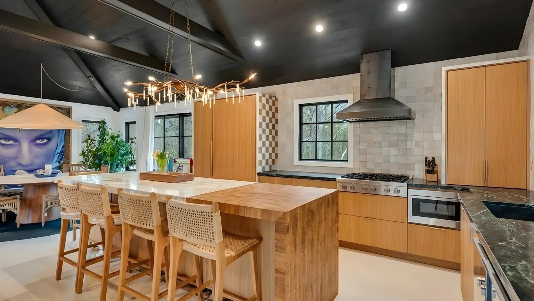 A spacious kitchen with a large island, wooden seating, and a range beneath a hood.