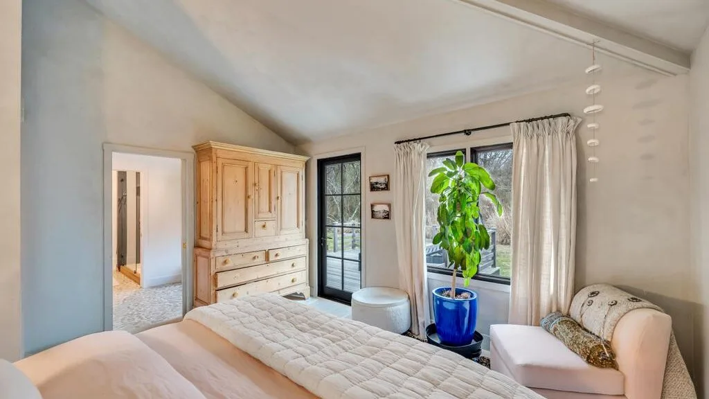 A bright bedroom with a large bed, a potted plant, and a window.