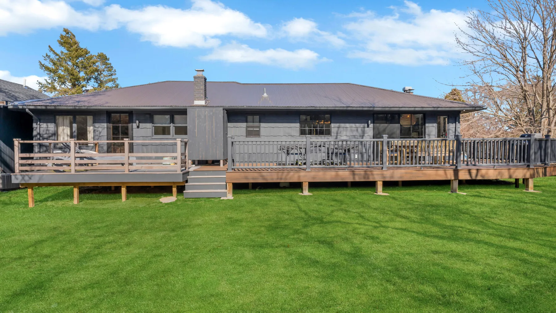 A low house faces a broad lawn, with a raised wooden deck along the facade.