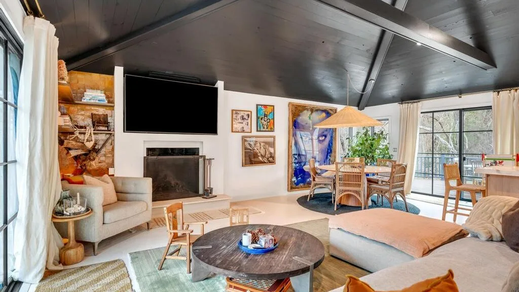A bright living room with a low round coffee table and a dining area by the windows.