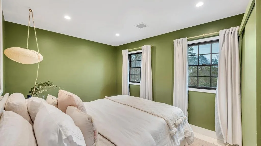 A bedroom with a large bed, green walls, and two curtained windows.