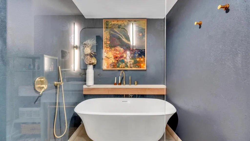 A bathroom with a freestanding bathtub beneath colorful abstract artwork.
