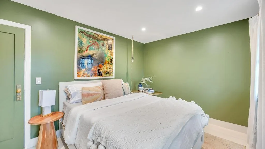 A bedroom with a neatly made bed and colorful artwork on the wall.