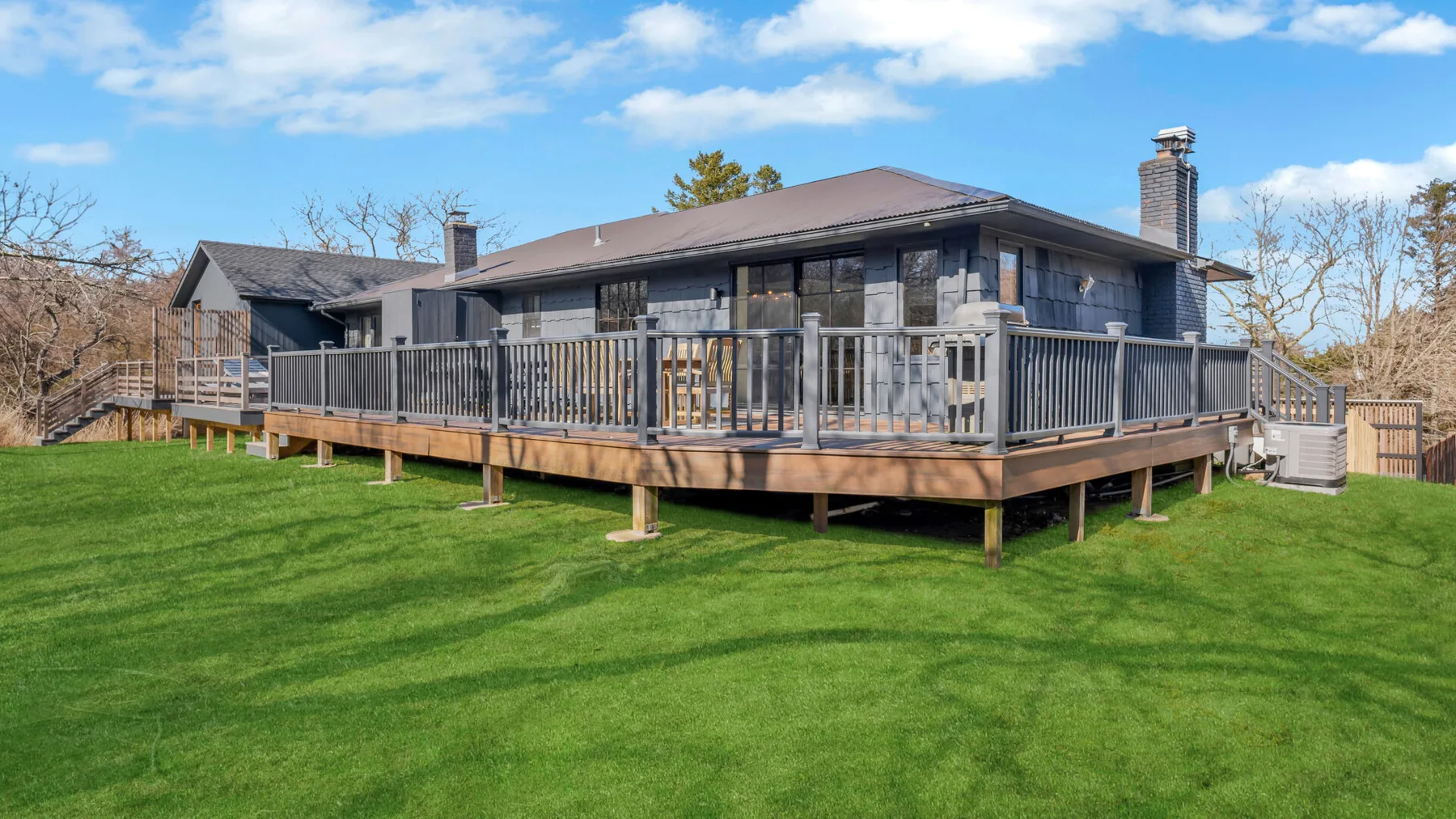 A house with a raised wooden deck overlooking a broad green lawn.