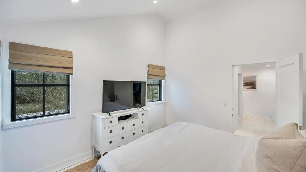 A bright bedroom with a bed, television, and windows with blinds.