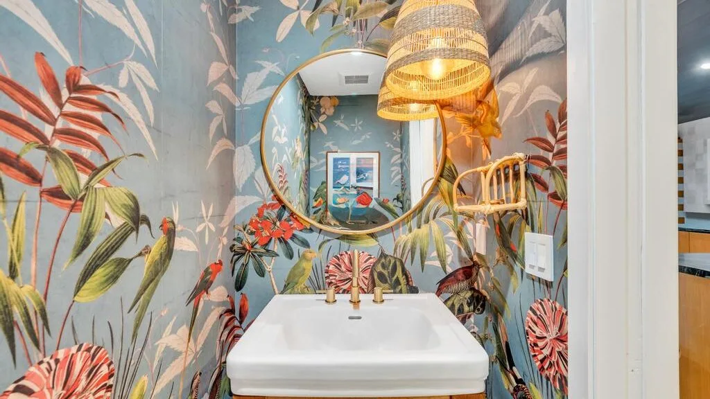 A bathroom vanity with a sink and round mirror against colorful botanical wallpaper.