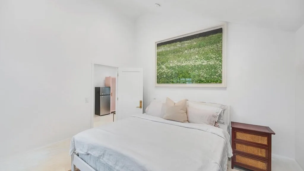 A bright bedroom with a neatly made bed and a framed landscape image.