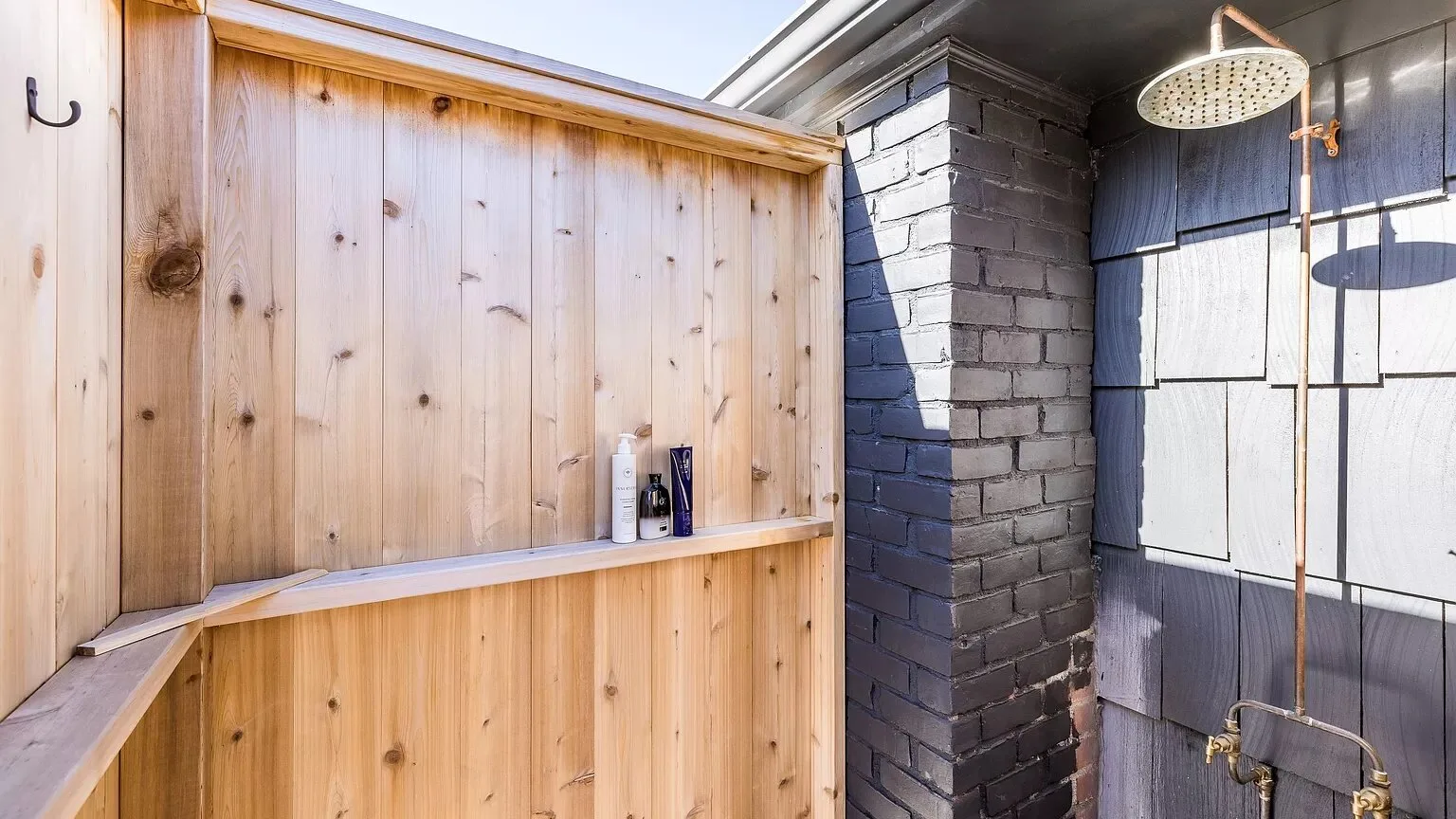 An outdoor shower area with a wooden privacy screen and dark tiled walls.