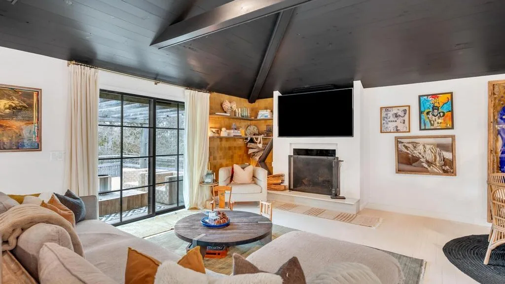 A living room with seating, a coffee table, and a fireplace beneath a sloped ceiling.