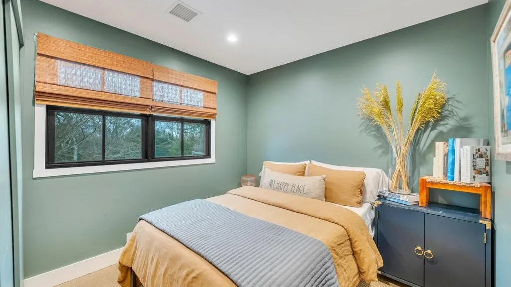 A bedroom with a bed beneath a window and a cabinet beside it.
