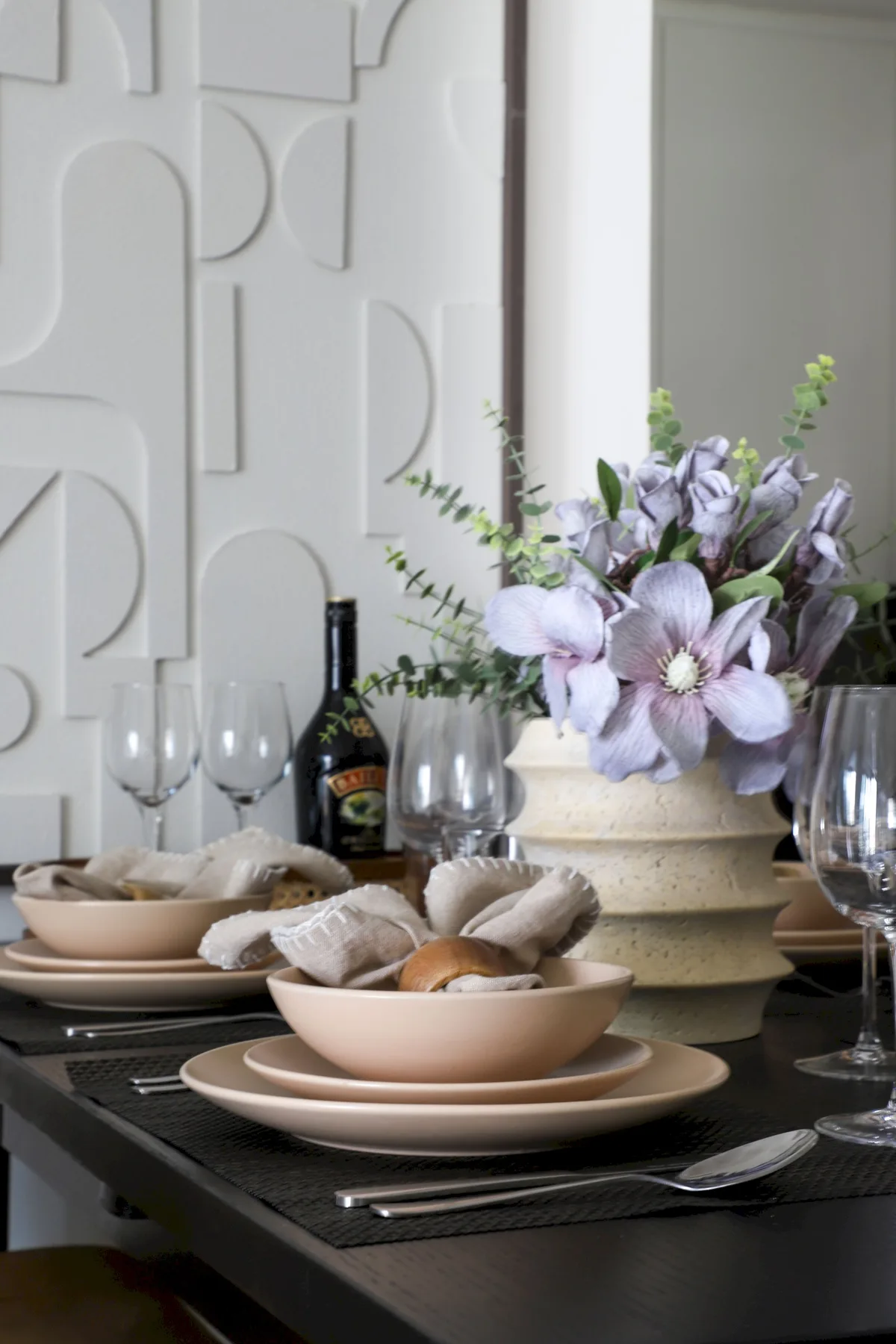 Una mesa de comedor está puesta con platos, copas y un jarrón de flores.