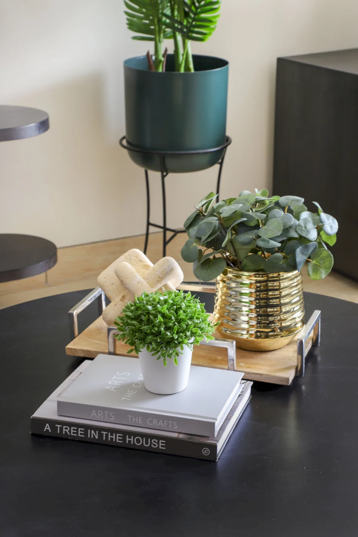 Una decoración de mesa presenta plantas en macetas, libros apilados y una bandeja decorativa.