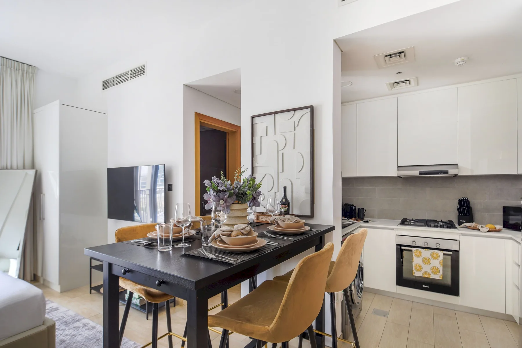 Un comedor se abre a una cocina luminosa, con una mesa y armarios blancos.