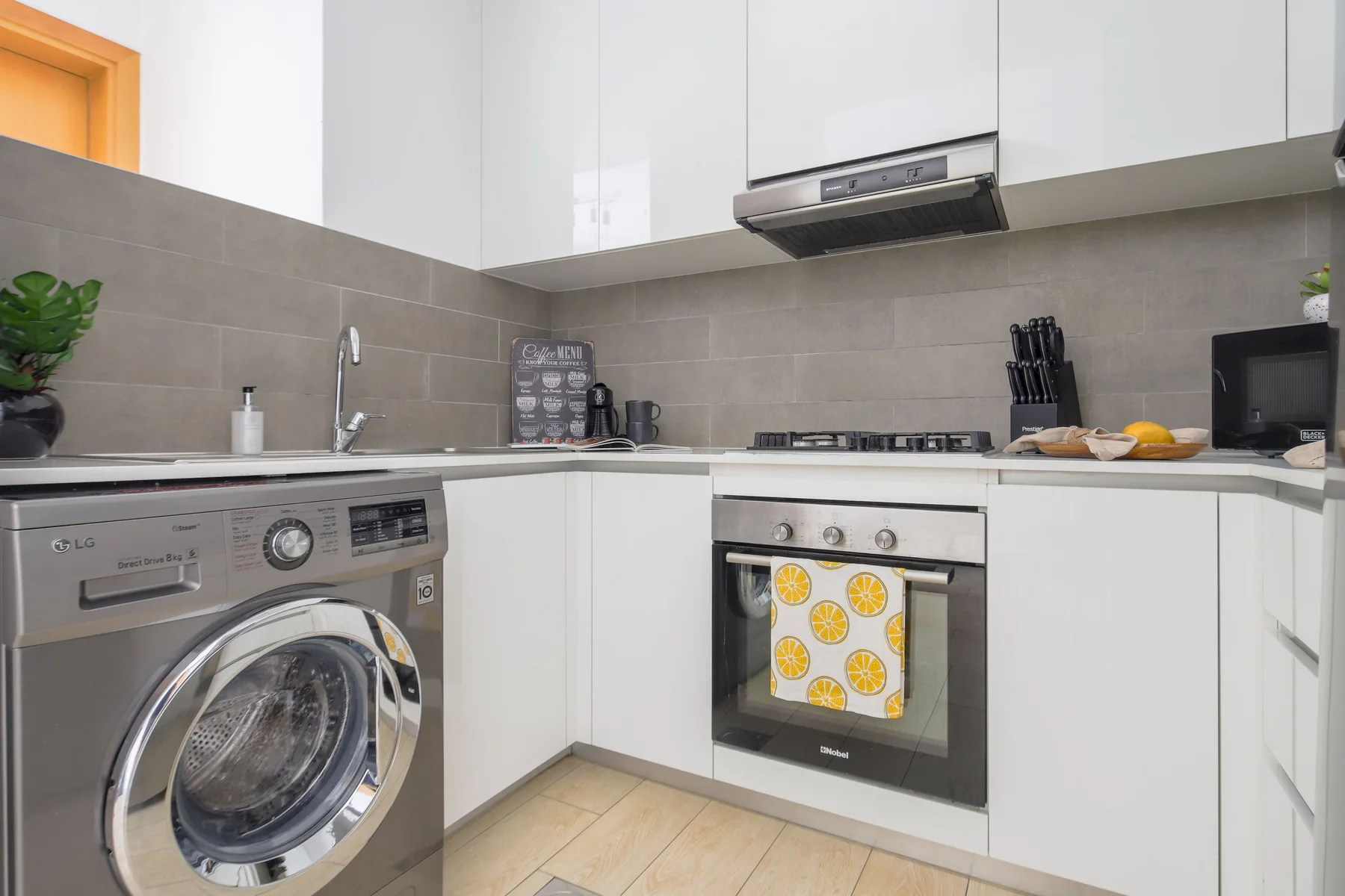 Una cocina compacta con gabinetes blancos, una placa de cocina y una lavadora.