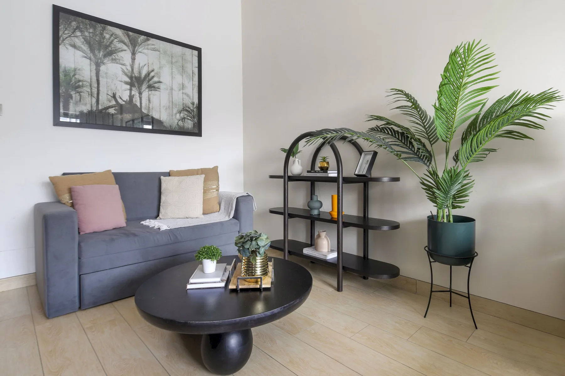 Una sala de estar con un sofá gris, una mesa de centro redonda y una planta en maceta.