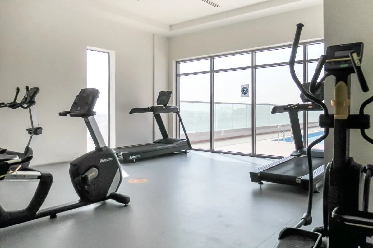 Una sala de ejercicio luminosa con cintas de correr y otros equipos junto a grandes ventanas.