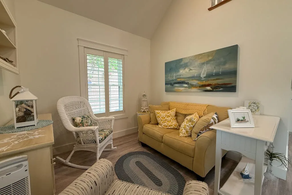 A living room with a mustard-colored sofa, a rocking chair, and a framed painting.