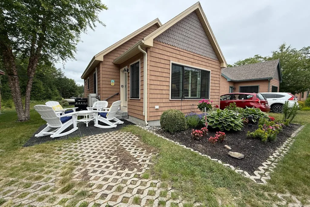 A small house with outdoor seating and a landscaped garden beside the driveway.