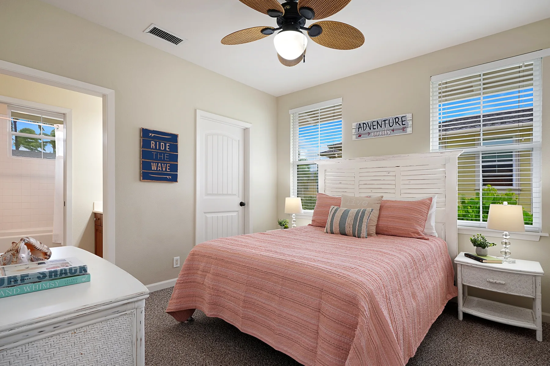 Un dormitorio con una cama rosa, cabecero blanco y ventanas con persianas.
