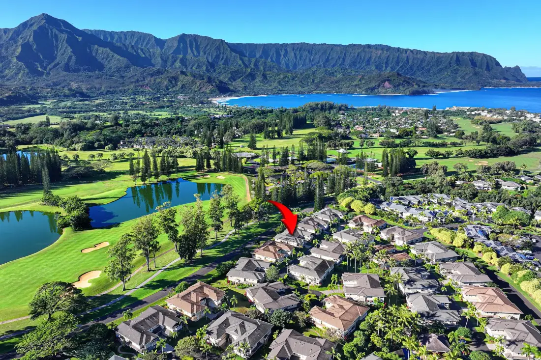 Vista aérea de viviendas junto a un campo de golf, con un lago y montañas al fondo.
