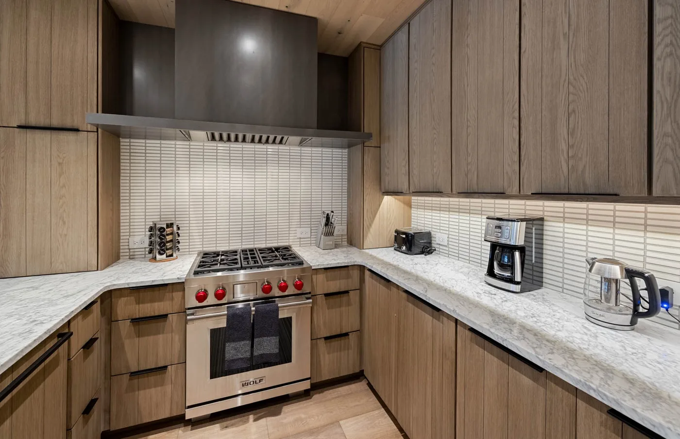 A modern kitchen with wood cabinetry, stone countertops, and a stainless steel range.