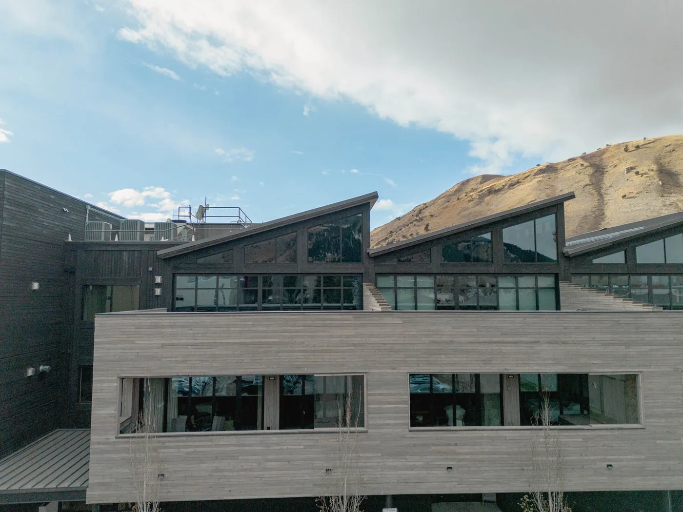 A modern building with dark angular rooflines stands against a dry hillside.