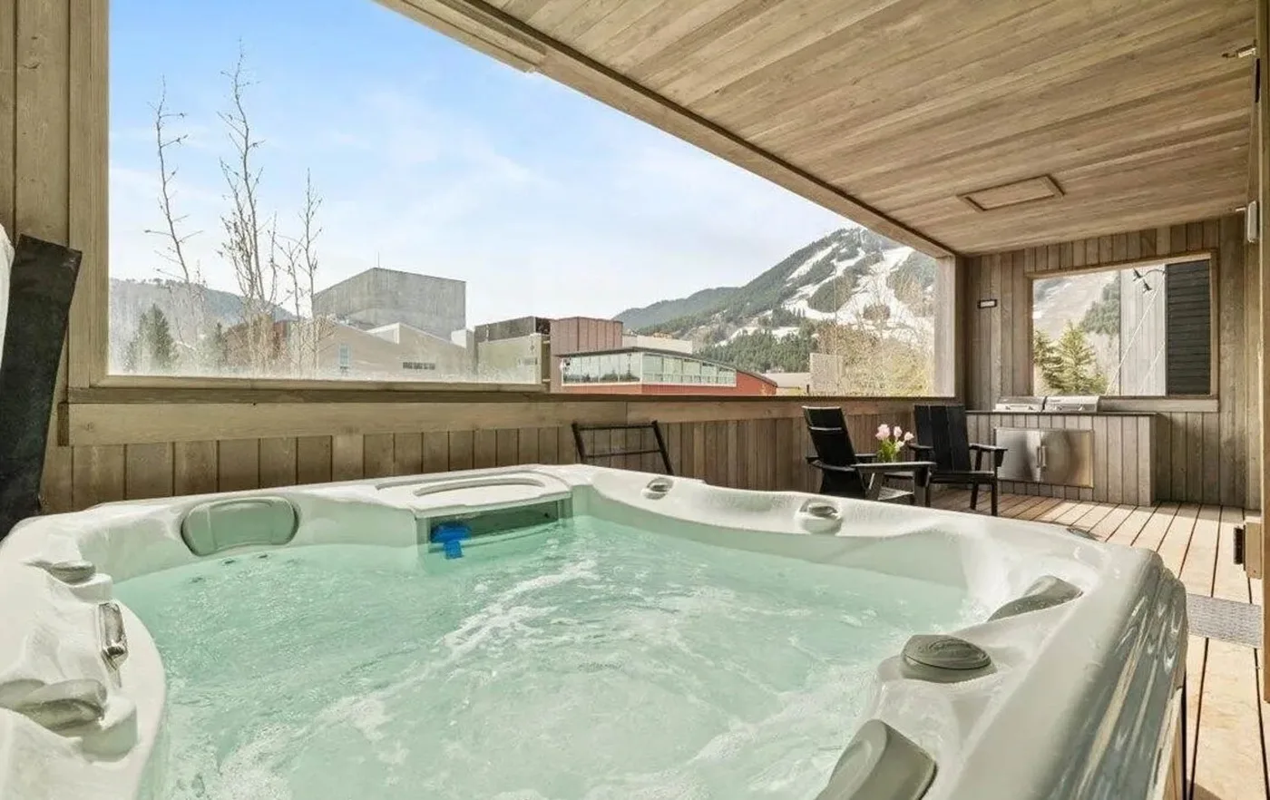A bubbling hot tub sits in an enclosed wooden room with mountain views.