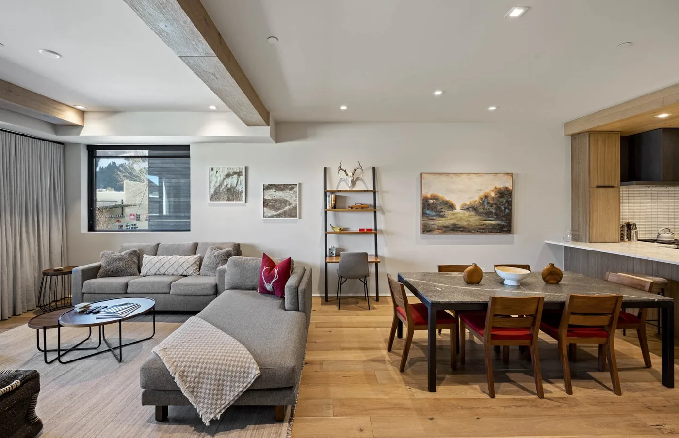 An open-plan living and dining area features a sectional seating area beside a wooden dining table.