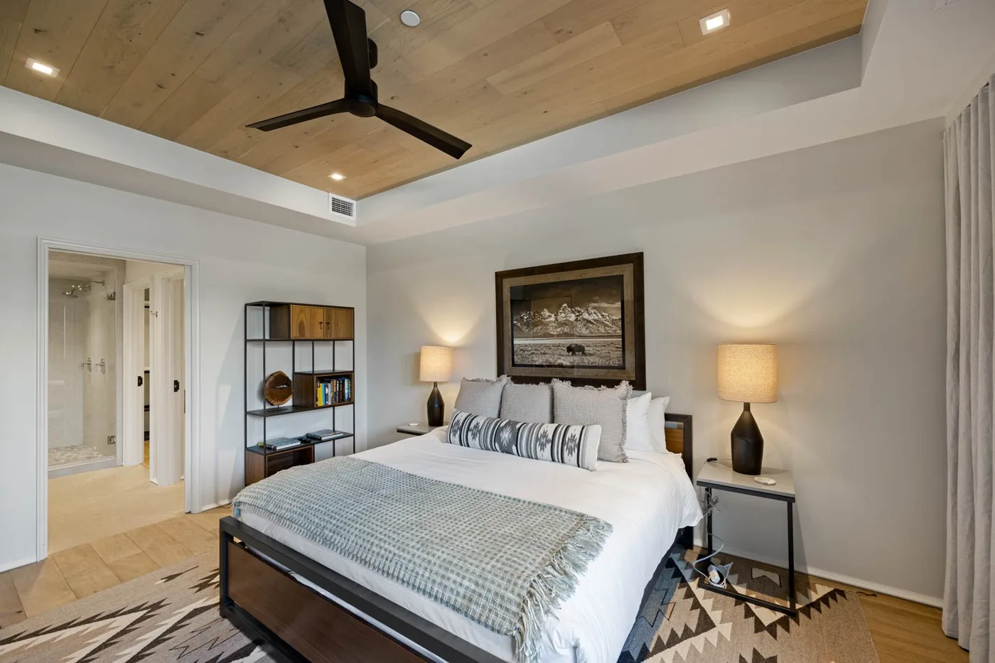 A bedroom with a neatly made bed, bedside lamps, and a ceiling fan.